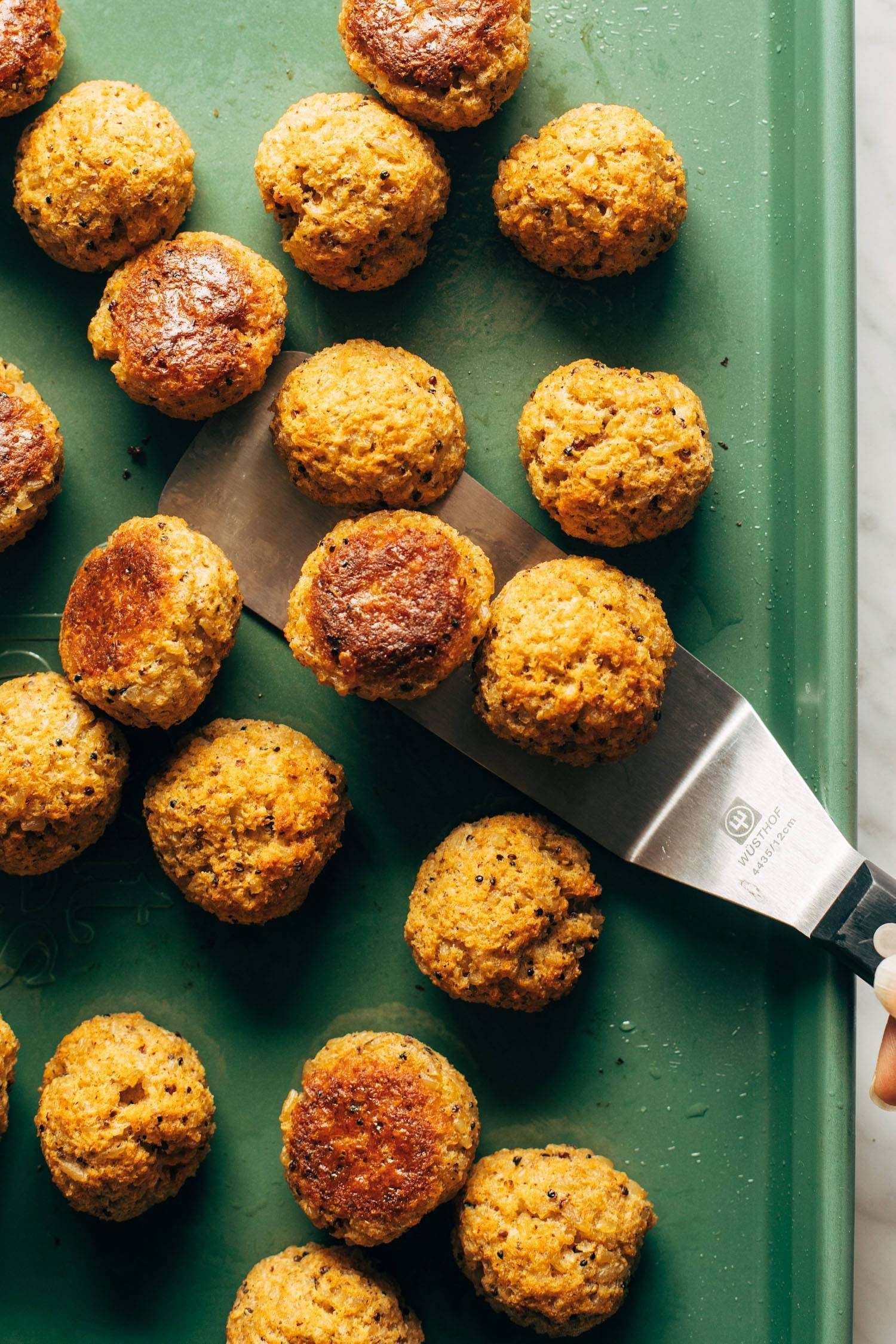 Cauliflower vegetarian meatballs on a sheet pan with a spatula.