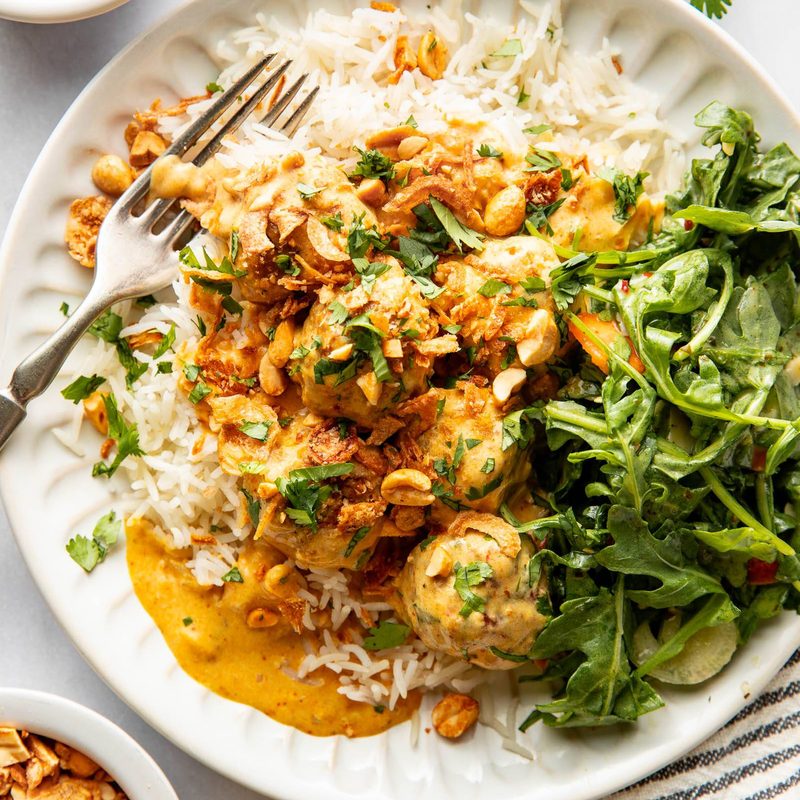 Yellow curry meatballs on a plate with rice and greens.